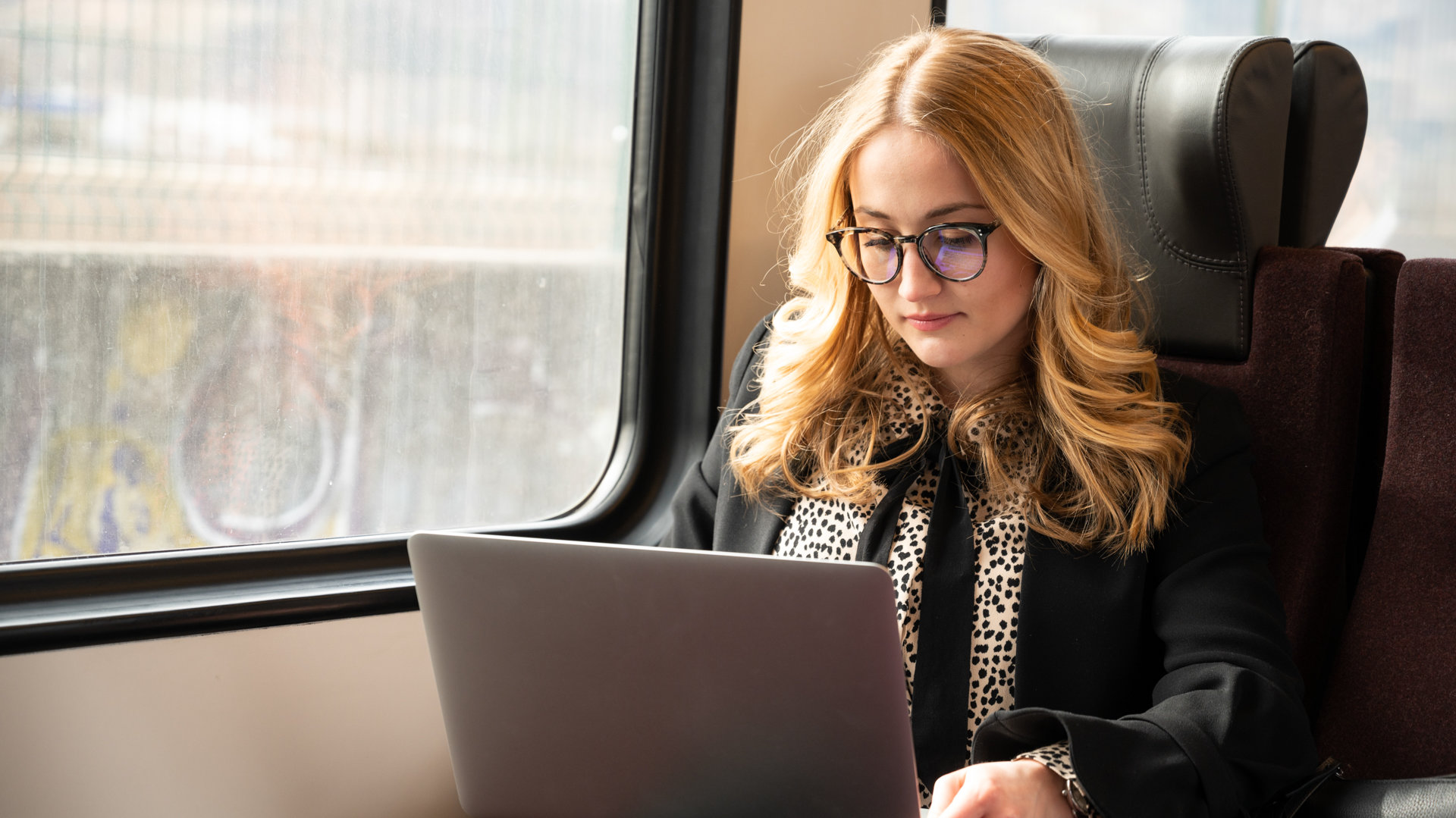 A girl with glasses working on her laptop on the train