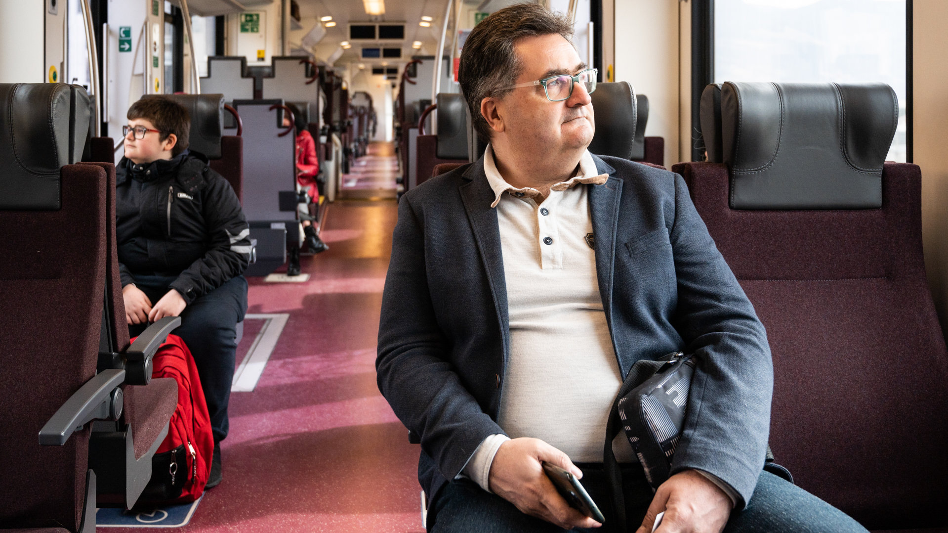A passenger with a smartphone in one hand is looking outside the train window.